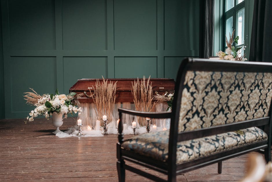 An interior scene featuring a polished wooden piano decorated with dried beige pampas grass and fresh white flowers arranged in a white vase on the left. Several small white candles in silver holders 