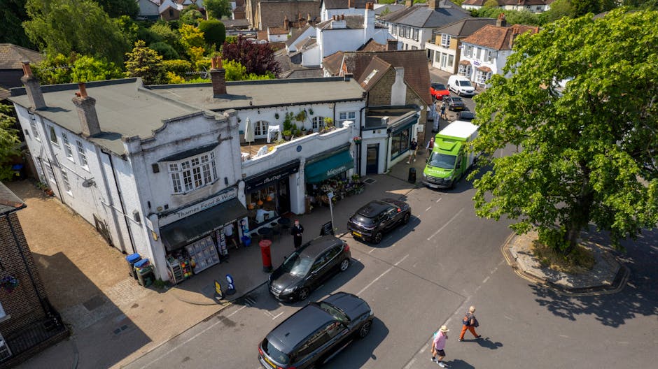 An aerial view of a small retail row in Grove Park SE12 featuring a florist shop with a white facade, green awning, and flower displays outside. Several fresh flower bouquets are visible through the s