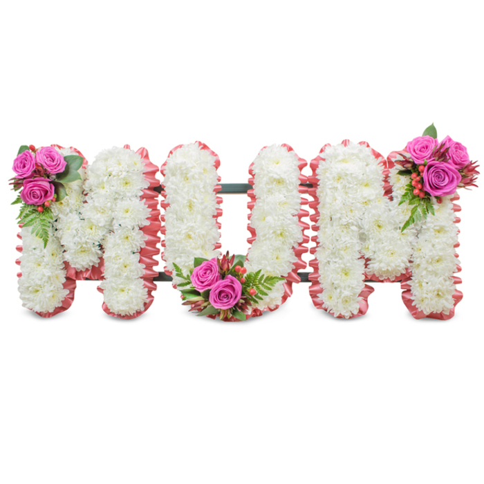 A poignant, lovingly constructed memorial piece spells out 'MUM' in three large capital letters, each letter expertly faced with a dense mass of immaculate white chrysanthemums that create a soft, textured plane across the face of the tribute. The chilly, satin-like whites of the mums are edged with a ruffled blush-pink ribbon which imparts a tender, maternal warmth to the overall composition; the pink trim gently defines each letter and offers an intimate contrast to the serene white blooms. A dark green support frame is discreetly visible between the letters, indicating the standing nature of the tribute and the careful workmanship beneath. Three small, coordinated bouquets punctuate the layout: a compact spray of vivid fuchsia-pink roses accompanied by glossy green fern foliage and tiny coral Hypericum berries adorns the upper left of the first 'M'; a mirrored cluster sits in the heart of the 'U' at its lowest curve; and the upper right of the final 'M' receives the third similar adornment, creating balanced visual anchors across the word. The interplay of textures - from the cushiony chrysanthemums to the velvety rose petals and the taut berries - invites a quiet, tactile memory, while the soft scent of fresh flowers suggests solace rather than spectacle. Crafted with the sensitivity of a local florist, this design by Flowers Grove Park is well suited for funeral services and memorials around Grove Park, near Grove Park station or local chapels and cemeteries in SE12, offering families a dignified and tender farewell to a beloved mother.