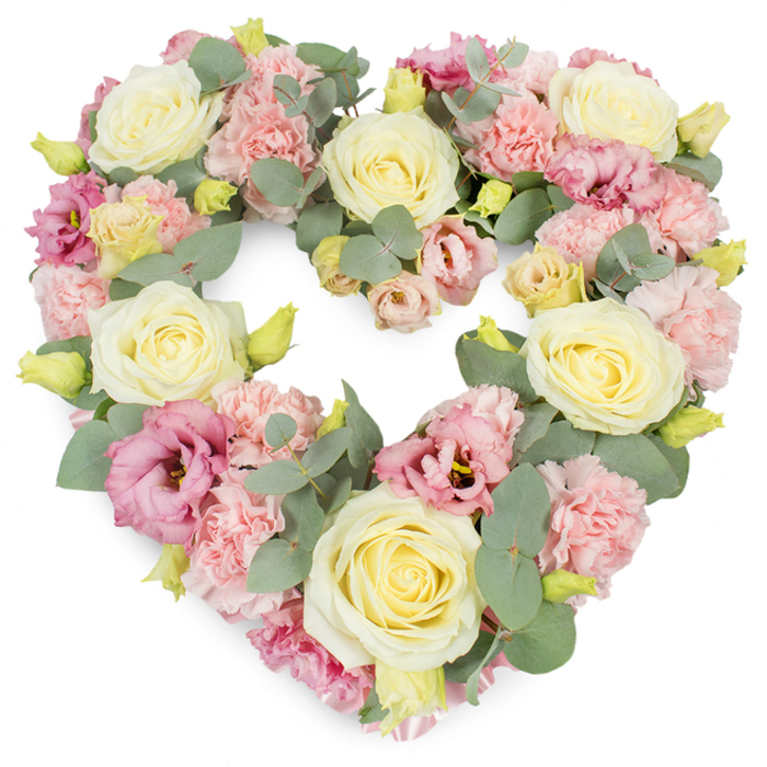 A full, heart-shaped wreath of pastel funeral flowers sits against a bright white backdrop, its shape instantly recognisable as a symbol of enduring love. The heart is created from a dense, carefully layered mix of blooms, dominated by velvety cream and soft lemon-yellow roses. Each rose is at a perfect stage of opening, with petals unfurling in gentle spirals that give a feeling of fullness without excess, lending the tribute a poised, elegant air. Interlaced among these are clusters of delicate, light pink carnations, their ruffled petals adding volume and a downy, almost cloud-like texture that softens the outline of the heart. Pockets of richer colour appear through the inclusion of deeper pink to mauve lisianthus flowers, whose more relaxed, cup-shaped blooms give movement and nuance, as though the arrangement holds layers of emotion. Threads of silvery eucalyptus foliage run through the composition, their rounded, muted green leaves providing both structural support and a cool, calming contrast to the warm floral tones. Tiny yellow-green buds peek from between petals, lending small sparks of freshness that suggest the continuity of life. The heart itself feels well-balanced and symmetrical, with a complete, flowing outline that would sit gracefully on an easel or stand at a Grove Park service, perhaps near the leafy avenues leading towards Chiswick or the riverside walks. This wreath's soft palette of cream, pink, and green evokes tenderness, sympathy, and a gentle farewell, making it a fitting tribute for funerals, memorials, or anniversaries when words are difficult. Crafted with the attention to detail you'd expect from Flowers Grove Park, it embodies both professional skill and quiet compassion.
