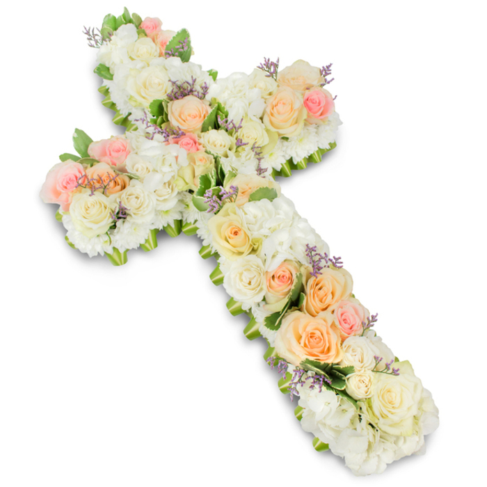 A large, cross-shaped floral arrangement is captured in a carefully lit studio setting, the bright white background highlighting every nuance of its pale, comforting palette. The cross has rounded edges and a fully padded surface, entirely covered by an intricate blend of white, cream, and pastel blooms. Full-sized roses in pure white and soft ivory are the most prominent, their layered petals unfolding in calm spirals, accompanied by clusters of fluffy white hydrangeas that fill any spaces, adding volume and a plush, quilted effect. Dancing through this snowy base are pearls of colour: soft peach roses, apricot buds, and light blush pink blossoms that seem to drift along the arms and centre of the cross, adding gentle warmth and drawing the eye. Fine touches of lavender-coloured filler flowers are sprinkled throughout, almost like a painter's final strokes, giving extra depth to the otherwise pastel design. Here and there, small shards of fresh green foliage peek out, subtly defining the outer edges and echoing the verdant feel of Grove Park's nearby green spaces and riverside walks. The lighting is even and calm, revealing the textures of each flower-the satin sheen of rose petals, the soft, cloud-like clusters of hydrangeas-and casting a delicate shadow beneath the cross that grounds it in three dimensions. Created as a sympathy tribute, this cross would sit beautifully at the front of a funeral or memorial service, symbolising enduring faith, love, and the hope of eternal rest. Flowers Grove Park could easily imagine delivering such an arrangement to a local chapel, where it would provide quiet comfort and a sense of the sacred to all who gather.