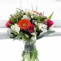An ode to Grove Park's natural beauty, this masterful floral composition speaks the language of harmony and joy. Creamy peach and soft beige gerberas form a halo of light at the bouquet's centre, their gentle petals radiating outward and complementing the bold zest of fiery orange gerberas beside them. Deep magenta roses, nestled thoughtfully throughout, anchor the palette with a note of rich sophistication. White alstroemeria and delicate spray roses provide crisp, sparkling highlights, their small, layered blooms adding texture and airiness evocative of Grove Park's peaceful leafy avenues. Broad, mirrored aspidistra leaves curl protectively around the stems, creating a lush, tranquil collar that shapes and fortifies the design. Slender, pointed leaves and whimsical tendrils fill the spaces between blooms, giving the arrangement depth and energy. Resting in a tall, clear glass vase, the bouquet's leafy stems are visible, reinforcing the sense of organic abundance and freshly cut splendour. Warm, diffused daylight-like that coming through a riverside window-bathes the bouquet, gently revealing each colour and nuance without overwhelming their natural charm. The subtle scent of lilies and rose, imagined in the air, brings to mind strolls through nearby Dukes Meadows. Designed to bring optimism to gatherings, homecomings, or milestones along Bolton Road, this bouquet from Flowers Grove Park is a testament to the area's flourishing floristry and sense of community.